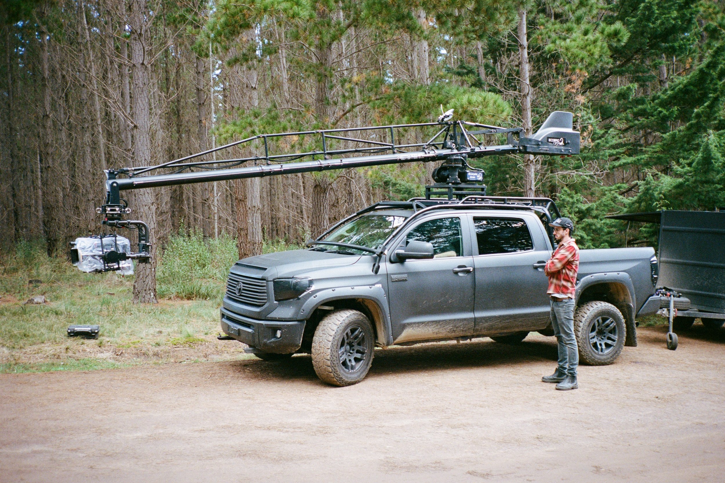 A camera car with a crane arm parked among pines, the still used for Production.
